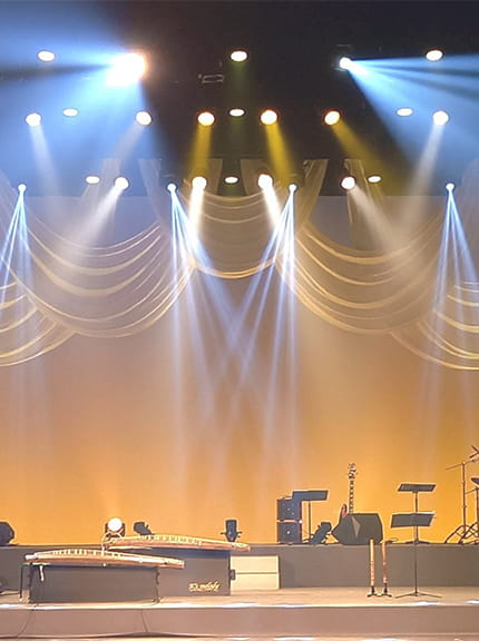 コンサートホールのステージで、淡い黄色や青色の照明をあてて、調整している様子